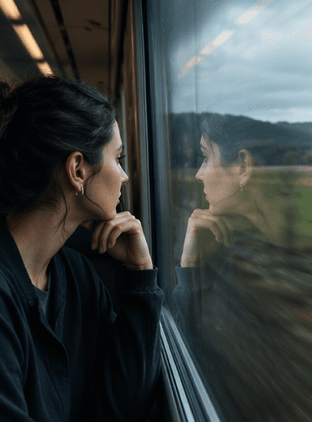 A woman on a train looking out the window, her reflection visible in the glass